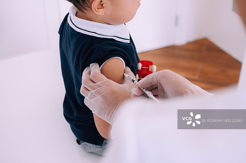 一位年轻的男医生正在给一位蹒跚学步的男婴注射疫苗图片素材