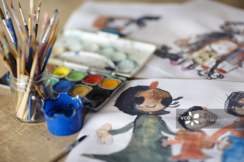 孩子画的一个家庭在一个装满画笔和调色板的罐子旁边的桌子上图片素材
