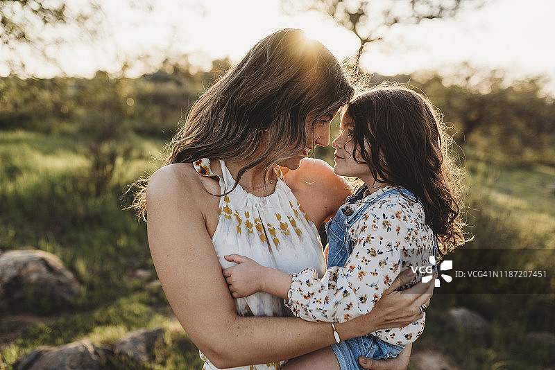 年轻的母亲抱着女儿，拥抱在明亮的加州田野里图片素材
