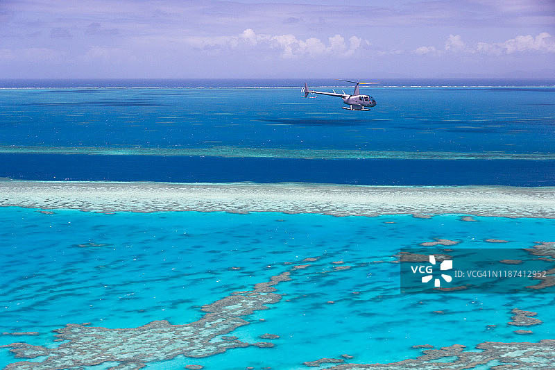 一架直升机载着游客飞过大堡礁，水面上是地平线。图片素材