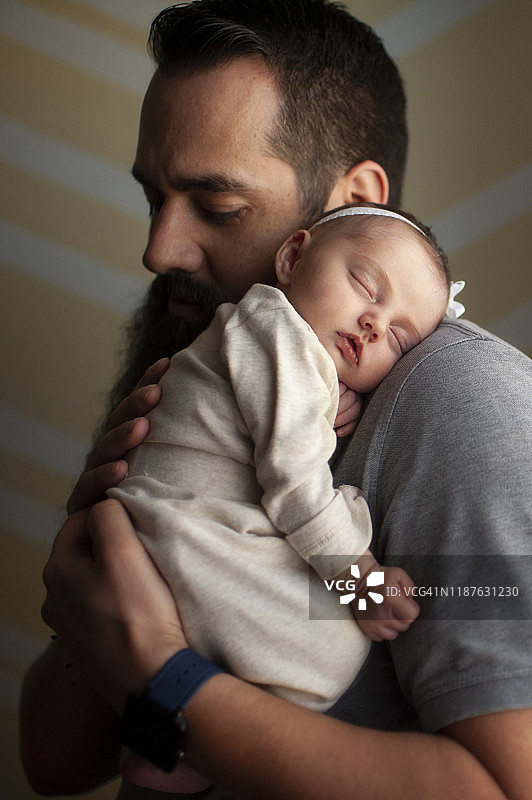 在家里，刚出生的女婴在柔和的光线下睡在父亲的肩膀上图片素材