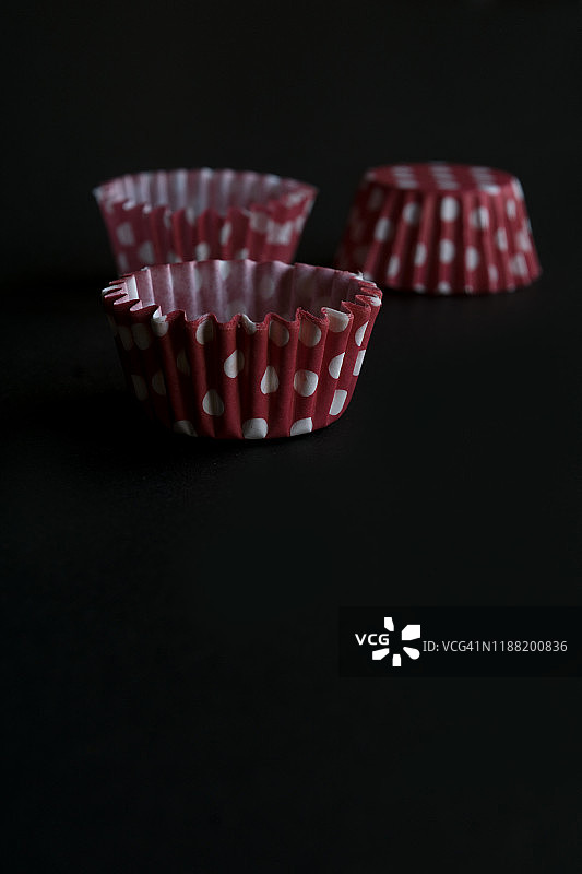三个红色和白色圆点纸杯蛋糕容器在黑色的背景。选择性聚焦和复制空间。图片素材
