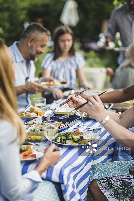 周末聚会期间，在后院与朋友和家人一起用餐的妇女图片素材