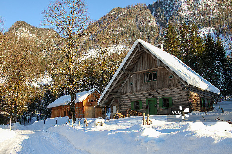漂亮的高山小木屋，前面有一堆被雪覆盖的木头。欧洲阿尔卑斯山的典型场景，以山脉和树木为背景。图片素材