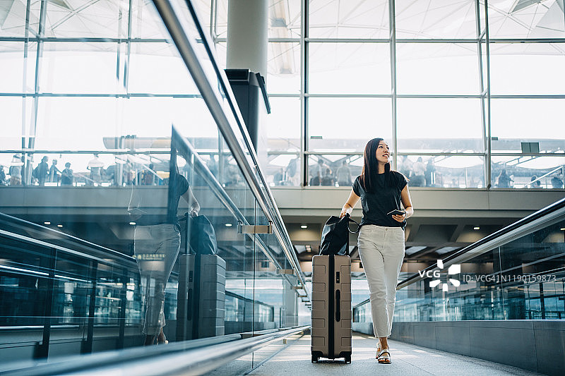 年轻的亚洲女子拿着护照和手提箱走在机场大厅图片素材