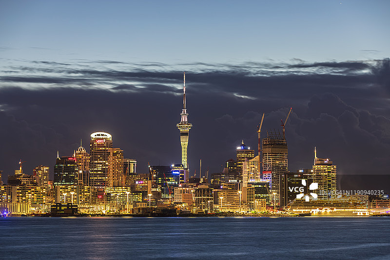 在新西兰大洋洲的黄昏，在多云的天空下，照亮了海上的现代建筑图片素材