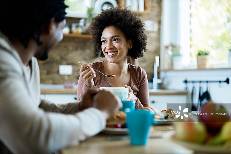 一个快乐的黑人女人在家里吃早餐的时候和她的男朋友聊天。图片素材