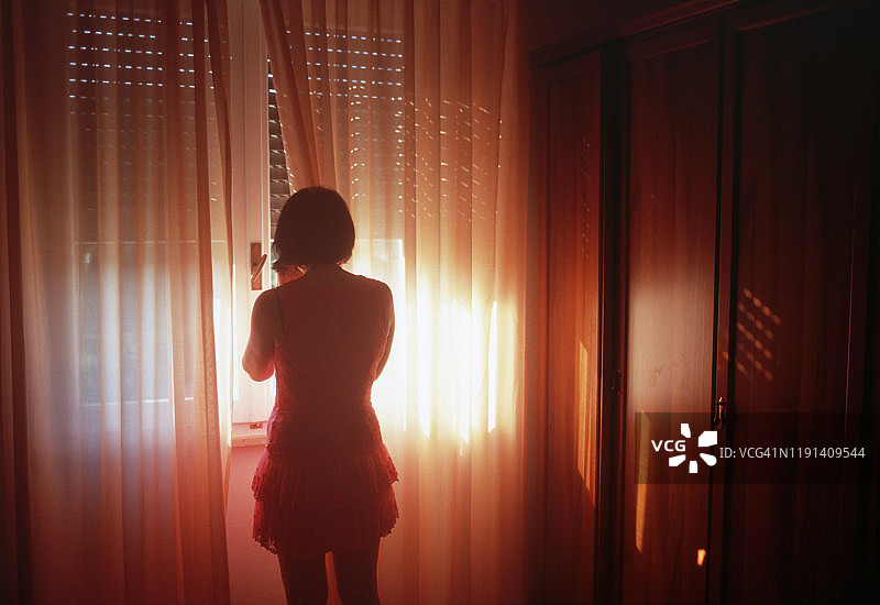 一个女人站在一扇挂着漂亮窗帘的窗户旁图片素材