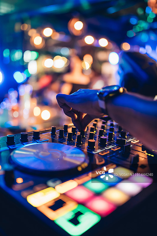 专业的DJ在海滩夜总会的舞台上，在转盘上演奏现场的布景和混音音乐。在俱乐部派对的混音台播放Jokey Hands。DJ混音控制器面板播放音乐和聚会。图片素材
