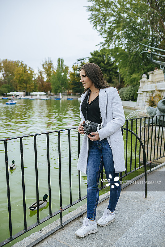 在西班牙马德里的埃尔雷蒂罗公园，一个女人拿着相机站在湖边图片素材
