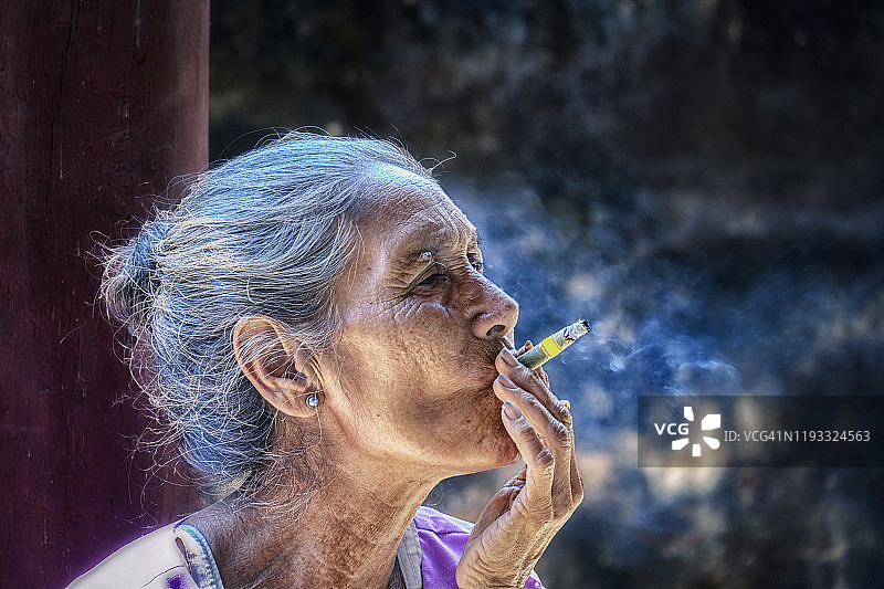 老妇人正在吸烟，在美丽的阳光下看起来不健康图片素材