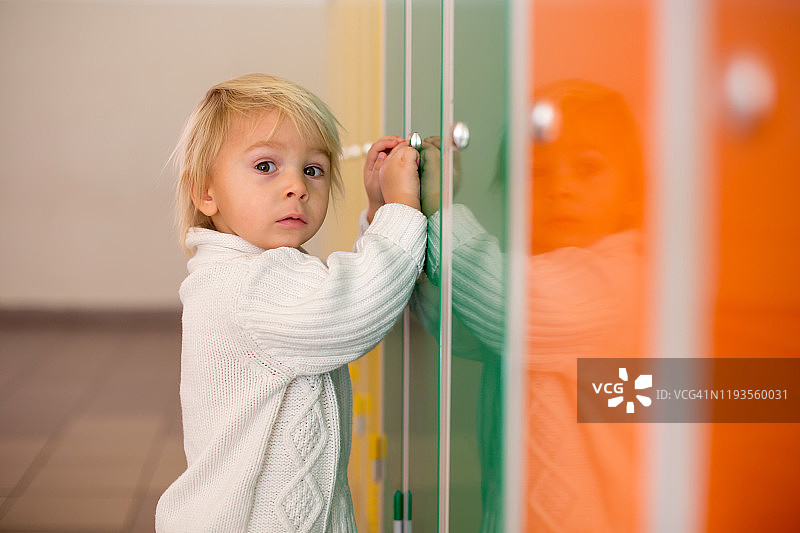 可爱的金发小男孩站在幼儿园或学校走廊的储物柜前图片素材