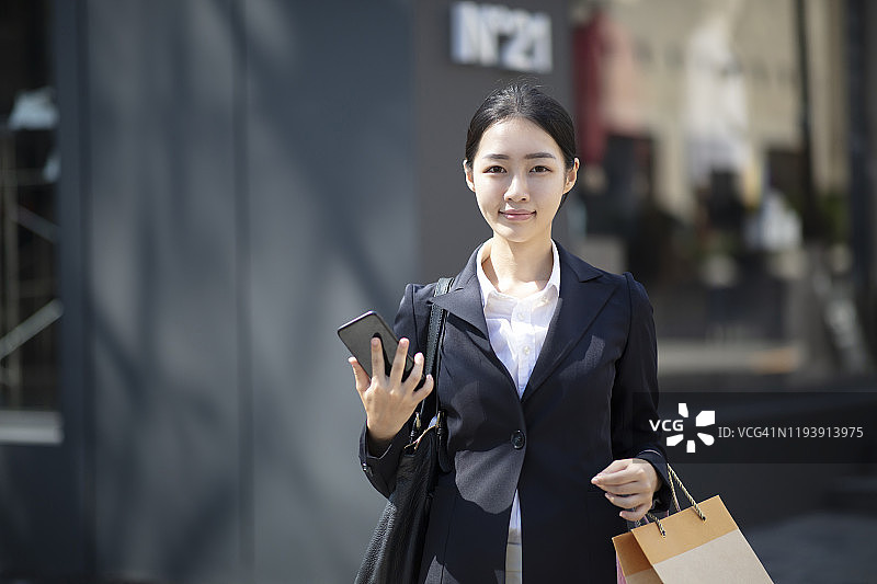 一名年轻女子在户外拿着智能手机拎着购物袋图片素材