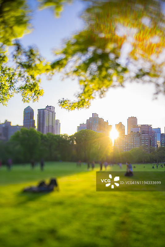 2019年5月11日，在美国纽约市中央公园，落日余晖照亮了公园内的建筑、绿树和人。图片素材