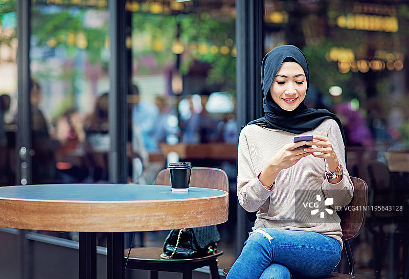 一名马来西亚女子在一家自助餐厅边喝咖啡边发短信图片素材