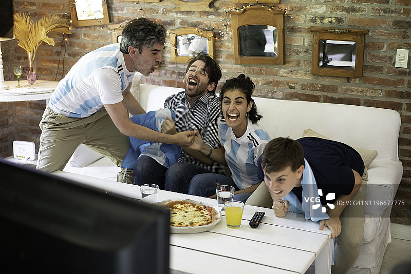 阿根廷球迷兴高采烈，尖叫着吃着外卖披萨，看着足球比赛图片素材