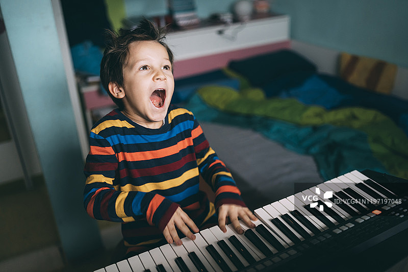 快乐的小男孩在家里一边弹数字钢琴一边唱歌图片素材