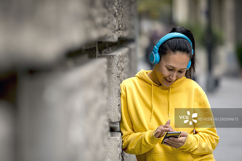 微笑的年轻女子穿着运动服，带着便携式信息设备和耳机在城市户外图片素材