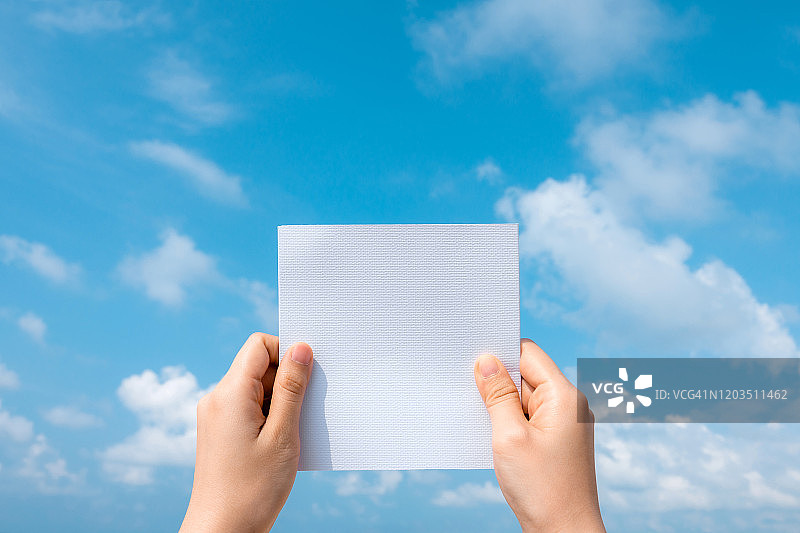 女人手握白纸，蓝天白云为背景。图片素材