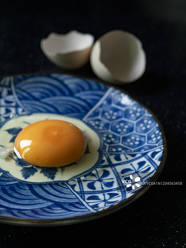 在黑色背景的盘子上放碎鸡蛋壳和生鸡蛋。图片素材