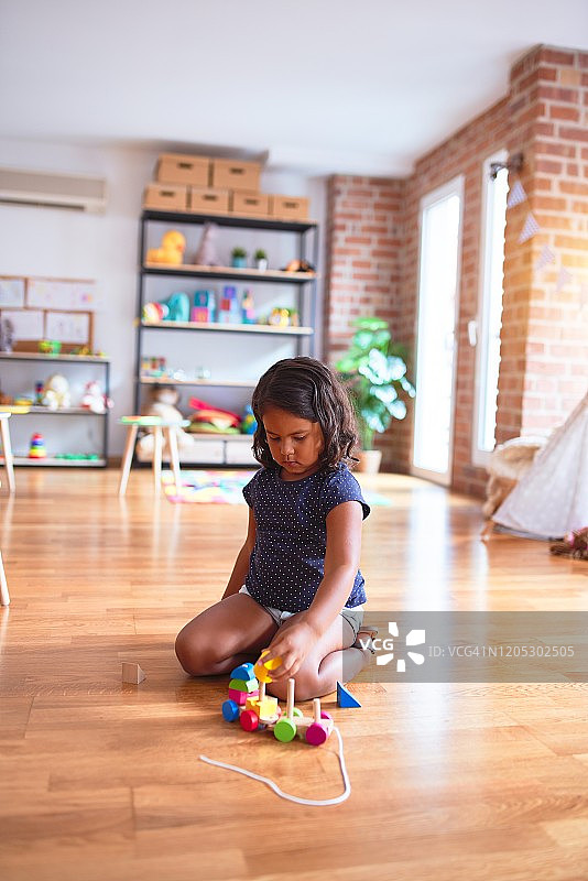 美丽的学步女孩坐在地板上玩火车在幼儿园图片素材