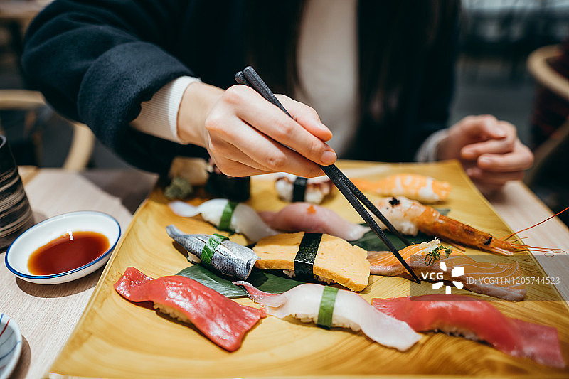 近距离的年轻亚洲女子吃新鲜制作的寿司与筷子在日本餐厅图片素材