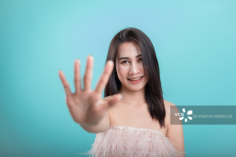 亚洲女孩做停顿手势，伸出手站在蓝色背景上。图片素材