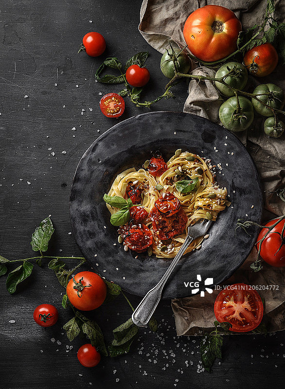 素食意大利面，焦糖洋葱，烤番茄和芝麻，在一个黑色粘土工艺盘上，深色纹理背景俯视图图片素材