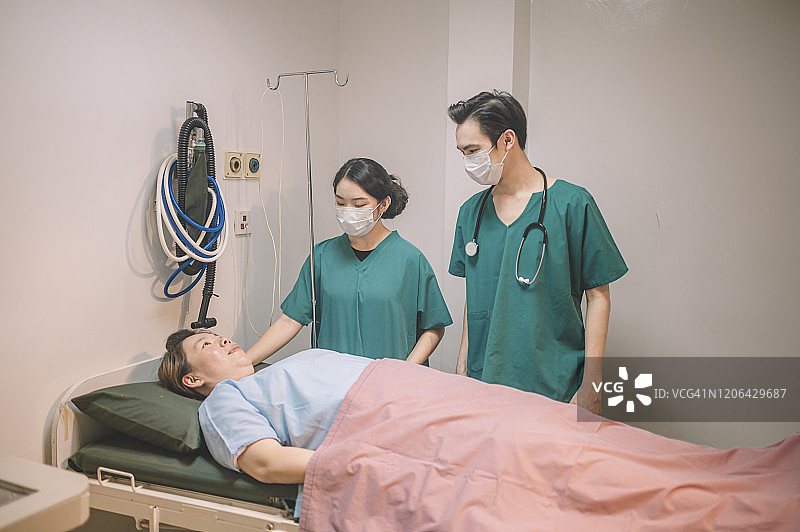 在医院的手术室里，一名亚裔华裔男医生、外科医生和女护士正在为手术做准备，并用毯子盖住病人图片素材