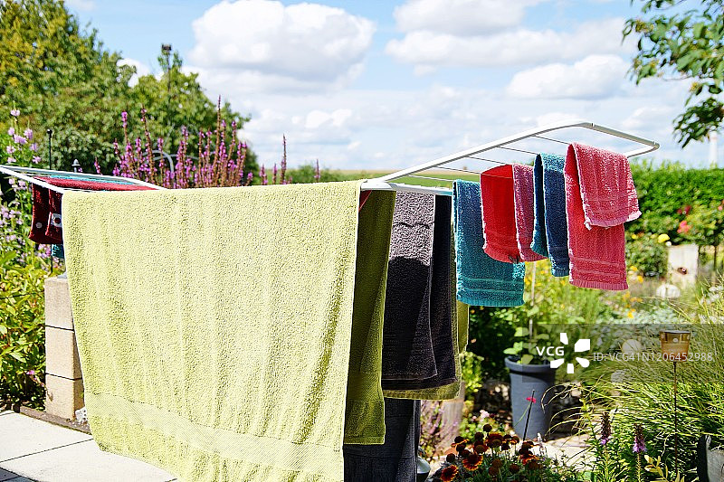 架子烘干机站在阳台上，在晴朗的日子里晾干各种颜色的毛巾。可折叠的衣服马在蓝天白云的背景图片素材