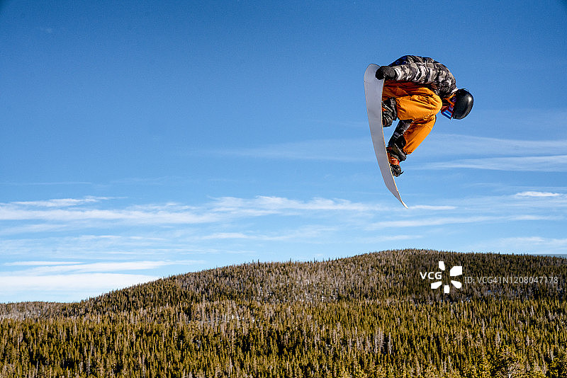在一个阳光明媚的日子里，一个年轻的男性滑雪板运动员在科罗拉多州的一个滑雪场跳下来图片素材
