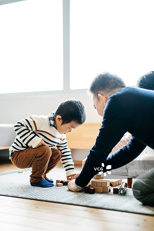 快乐的亚洲祖父母坐在客厅的地板上和小孙子一起玩积木图片素材