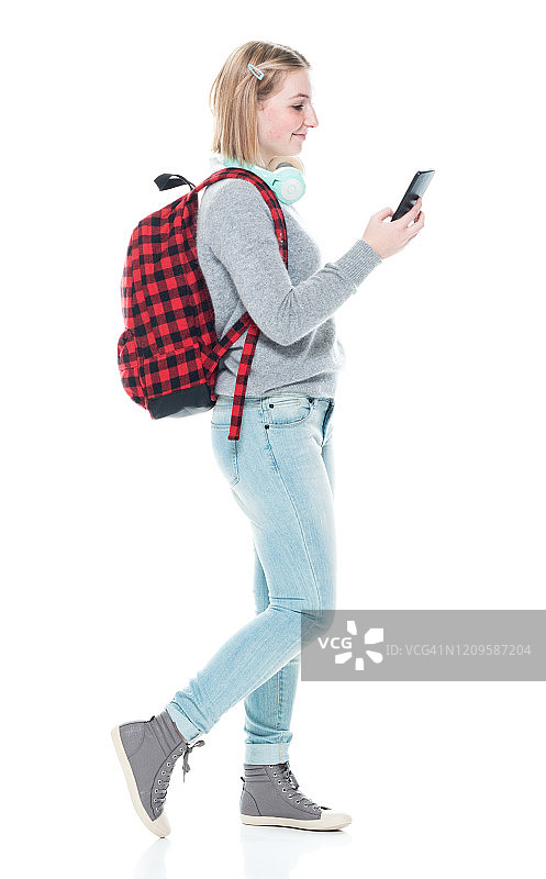 z一代女学生穿着裤子，拿着包，戴着耳机站在白色背景前图片素材