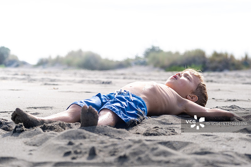 一个小男孩躺在沙滩上图片素材