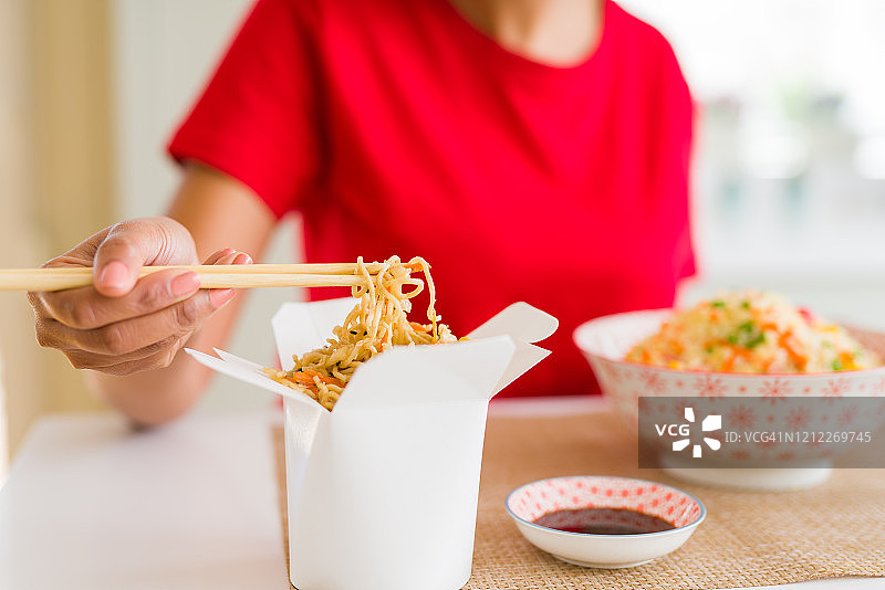近距离的年轻女子吃面条从送盒使用筷子图片素材