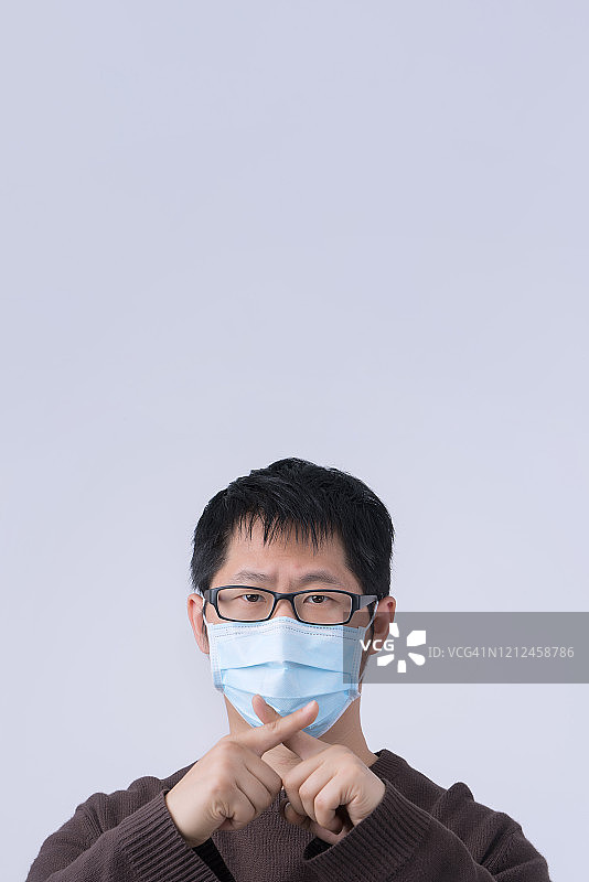 这是一幅年轻亚洲男子的肖像，他戴着医用外科蓝色口罩，在白色背景下隔离，向冠状病毒感染说不。图片素材