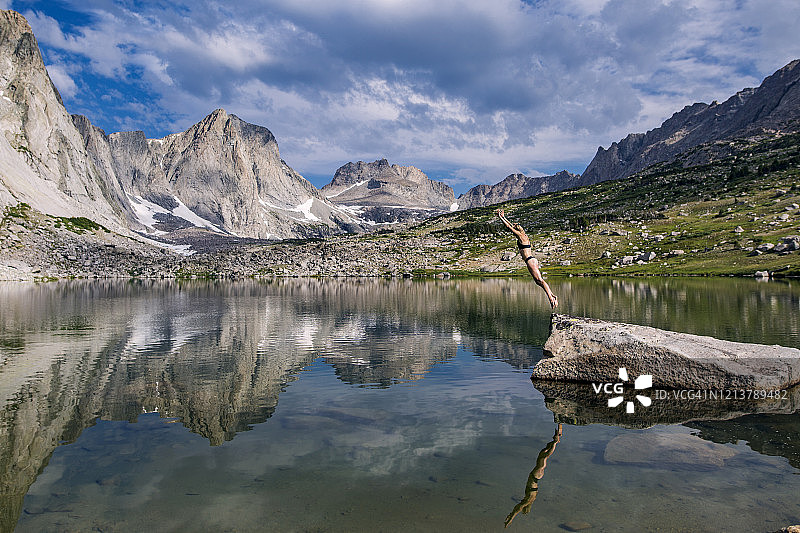 一个女人跳进一个质朴的高山湖泊和美丽的倒影图片素材