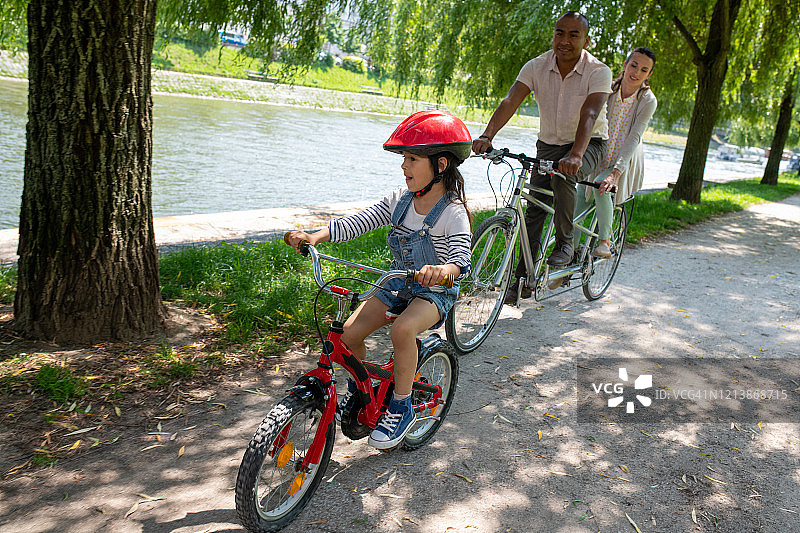 爸爸妈妈骑着双人自行车跟在女儿后面图片素材