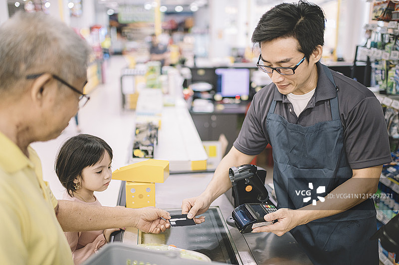 一位亚裔华人老人在超市柜台结账时向收银员付款图片素材