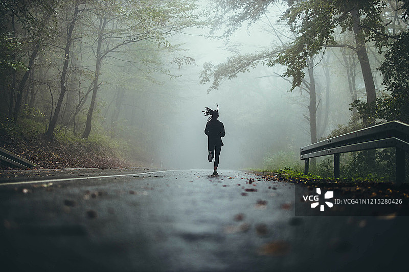 女运动员在迷雾森林的道路上奔跑的后视图。图片素材