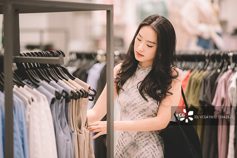 一位亚洲华人女性在服装店拿着购物袋买衣服图片素材