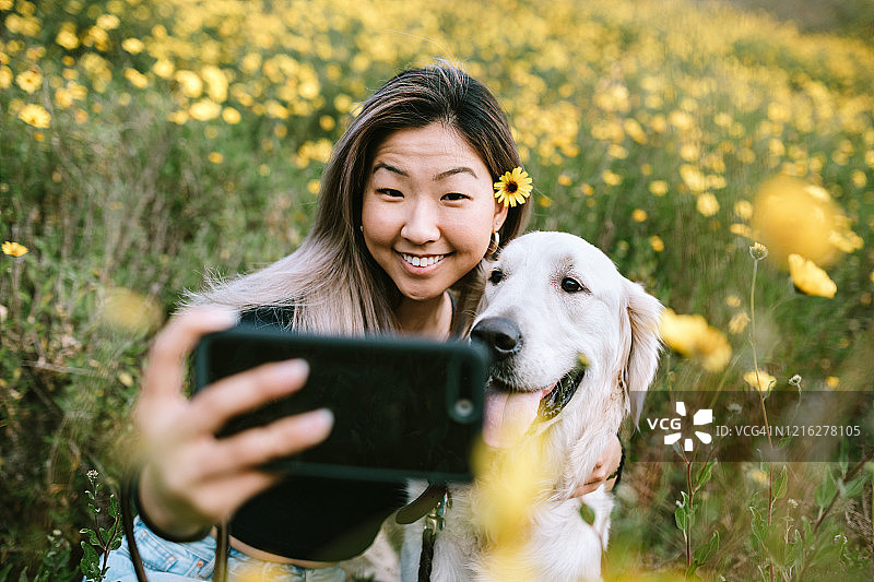 年轻女子与她的狗在鲜花盛开的田野自拍图片素材