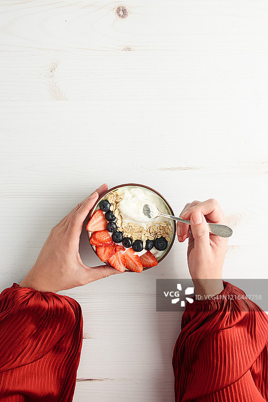 一个女人正在吃一碗酸奶，上面有新鲜的浆果，燕麦和蜂蜜图片素材