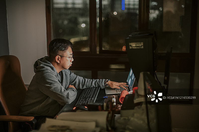 一个亚裔华人中年成年人在他的书房里独自工作，穿着连帽衫，坐在电脑前图片素材