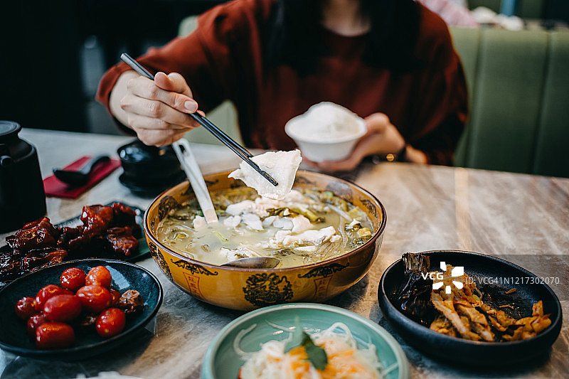 年轻的亚洲女子在餐馆里享受传统的中国四川菜，水煮鱼和酸菜以及其他各种菜肴图片素材