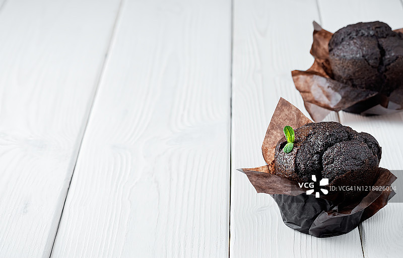 两个自制的巧克力松饼，装饰薄荷叶放在白色木桌上。关闭，复制空间图片素材
