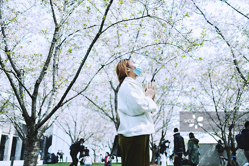 一位戴着面具的年轻女子在公园里双手合十图片素材