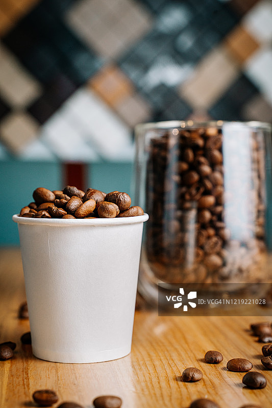 两杯烤咖啡豆-一个透明的杯子和一个小纸杯在咖啡馆的黑色和棕色的木桌上图片素材