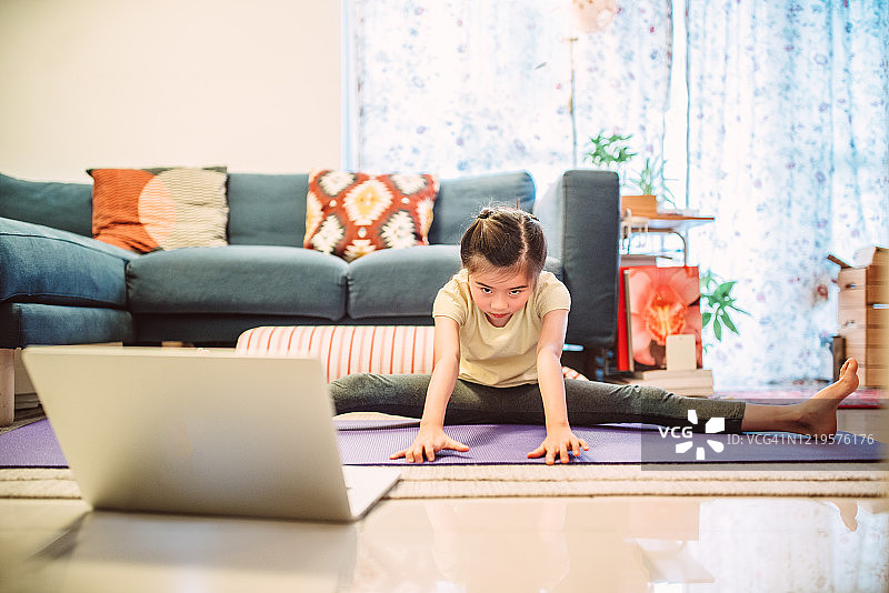 小女孩在家用笔记本电脑上在线瑜伽课图片素材