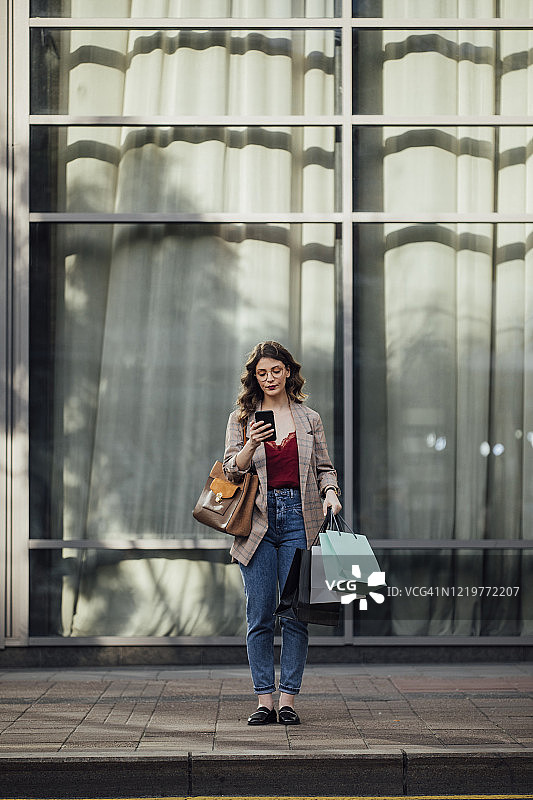 发短信和购物:一个女人在街上购物时用智能手机图片素材
